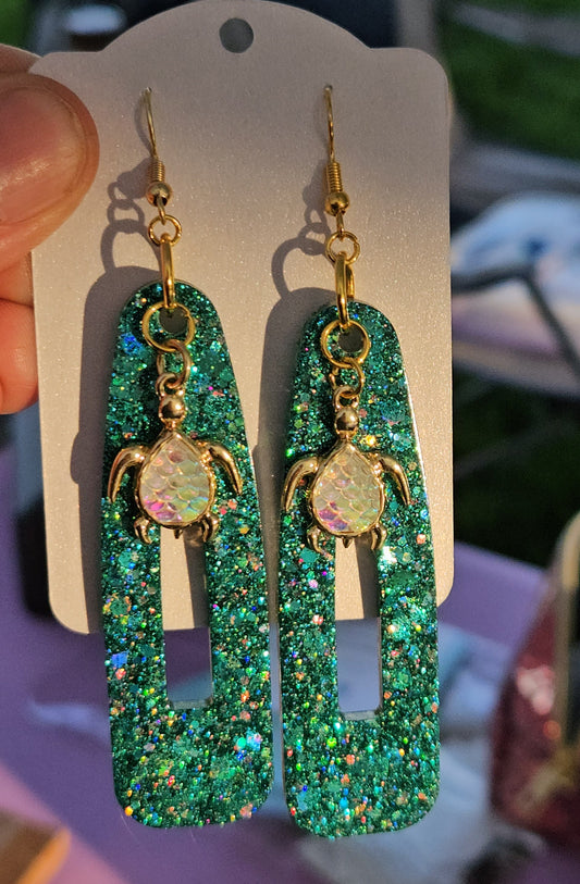 Green glittery earrings on a display card held by a hand with a blurred background