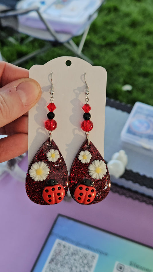 Teardrop-shaped earrings with red and black design held on a white card against a blurred background.