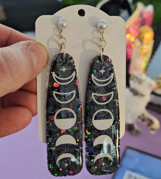 Pair of earrings with moon phase design held on a card against a blurred background